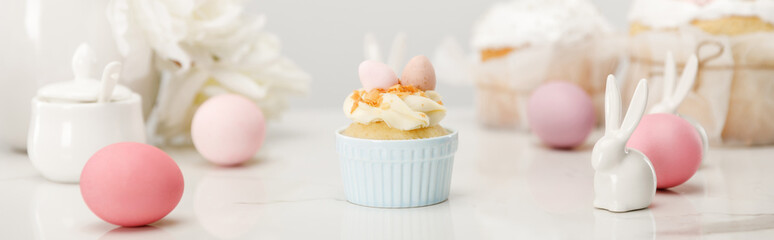 Selective focus of cupcake with colorful chicken eggs, decorative bunnies and sugar bowl on white background, panoramic shot