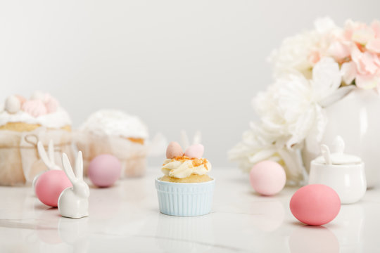 Selective focus of cupcake with colorful chicken eggs, decorative bunnies and vase with bouquet isolated on grey
