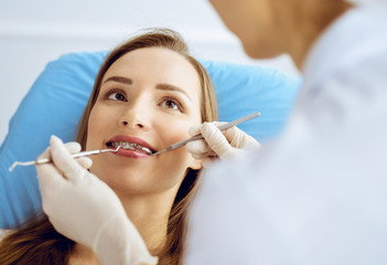 Smiling young woman with orthodontic brackets examined by dentist at dental clinic. Healthy teeth and medicine concept