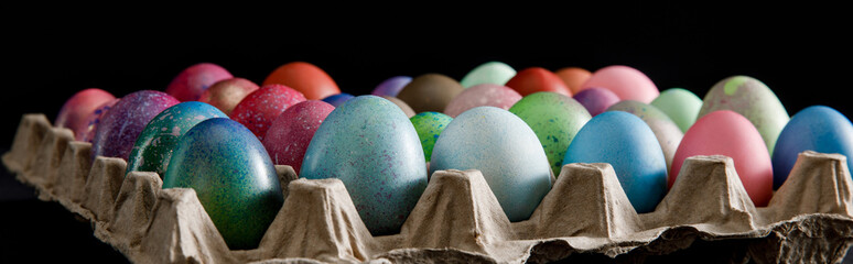 Selective focus of egg tray with colorful Easter eggs on black background, panoramic shot