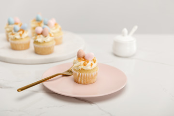 Selective focus of cupcakes on plate with fork and round board with sugar bowl on grey background