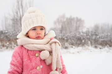 Obraz premium little girl in a purple coat, white hat and a large scarf is sad in winter during a snowfall