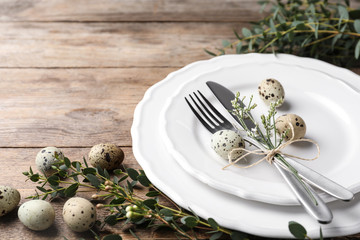 Festive Easter table setting with quail eggs and floral decor on wooden background, closeup