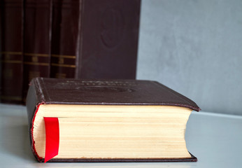old book with bookmark on a white table on a background of books