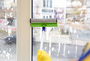 Professional young janitor in uniform cleaning window indoors, closeup
