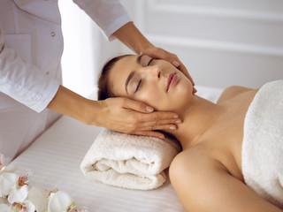 Fototapeta na wymiar Beautiful brunette woman enjoying facial massage with closed eyes. Relaxing treatment in medicine and spa center concepts