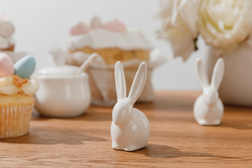 Fototapeta na wymiar Selective focus of decorative bunnies, cupcake, sugar bowl, and flowers on wooden background