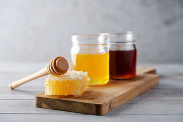 Fresh honey and honeycombs on wooden cutting board. Light floral and dark honey in glass jars