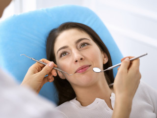 Smiling brunette woman being examined by dentist at dental clinic. Hands of a doctor holding dental instruments near patient's mouth. Healthy teeth and medicine concept