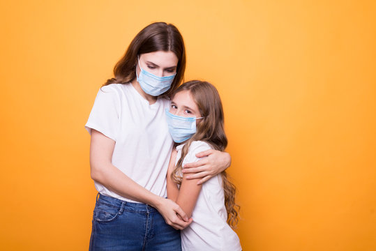 Sad Mother With Daughter In Medical Mask In Studio On Orange Background. Terrible Coronavirus Symptom