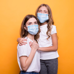sad mother with daughter in medical mask in studio on orange background. terrible coronavirus symptom