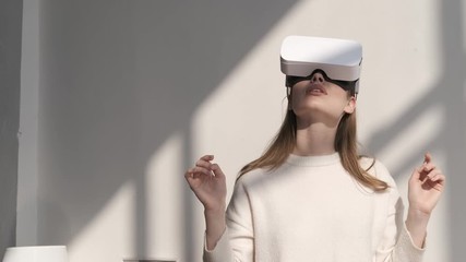 Young girl in living room playing in modern games using virtual reality glasses. Online education at home using VR AR modern technologies of the future. Happy cute woman touch something using 3D vr
