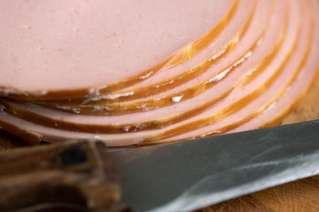 Slices of a tasty boiled sausage lying on the wooden cutting board with a knife