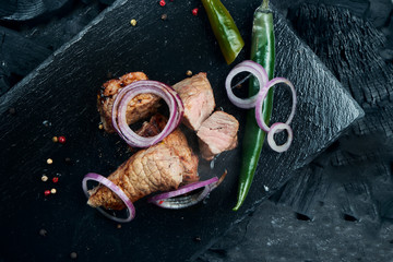 Appetizing beef kebab with spices and onions on a black slate tray on a background of charcoal. Shahlik. Close up portion of grilled meat