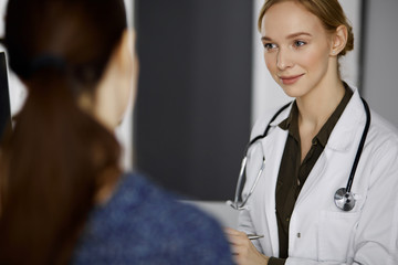 Cheerful smiling female doctor and patient woman discussing current health examination while sitting in clinic. Perfect medical service in hospital. Medicine concept