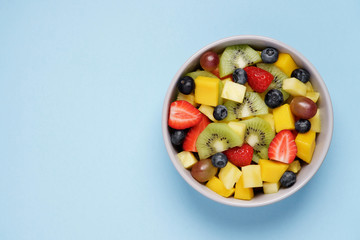 Fruit salad on bright blue background. Multi-colored ripe fruits and berries. Pineapple, mango, grape, strawberry, blueberry and kiwi