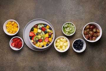 Fruit salad in bowl with ingredients. Multi-colored ripe fruits and berries. Pineapple, mango, grape, strawberry, blueberry and kiwi