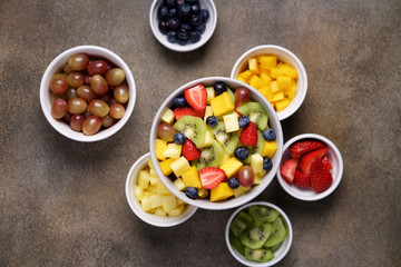 Fruit salad in bowl with ingredients. Multi-colored ripe fruits and berries. Pineapple, mango, grape, strawberry, blueberry and kiwi