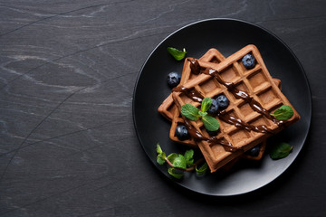 Belgian chocolate wafers decorated with mint and blueberries. Black background, top view