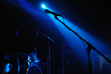 Completely dark empty stage with standing vocalist microphone silhouette and drums illuminated by unique 2 spot lights.