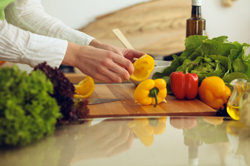 Unknown human hands cooking in kitchen. Woman slicing yellow bell pepper. Healthy meal, and vegetarian food concept