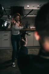 selective focus of creepy demoniacal girl with levitating cookware and exorcist with cross in...