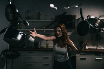 Fototapeta na wymiar creepy demoniacal girl with levitating pots and knives in kitchen