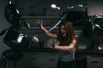 creepy yelling girl gesturing with levitating kitchenware in kitchen - obrazy, fototapety, plakaty