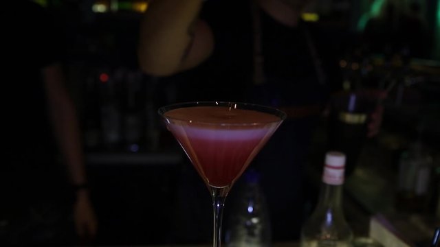 Hands bartender pours liquid through stainer inside cocktail glass. Bartender mixologist combining ingredients and making a tasty cocktail in a beautiful modern trendy bar.
