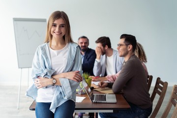 Beautiful young business lady looking at camera and smiling while her colleagues working in the background.