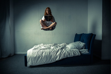 demonic woman in nightgown levitating over bed while reading bible