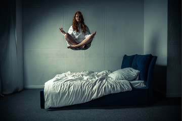 Obsessed girl levitating in lotus pose during meditation over bed