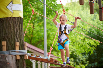 Little boy overcomes the obstacle in the rope park.