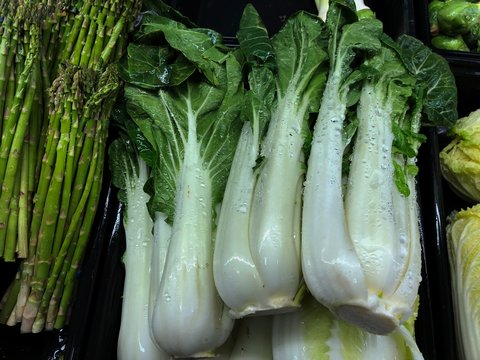 Asparagus and Chinese cabbage wet with water at the fresh produce section of a grocery store.