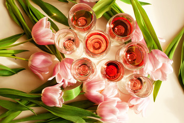 Glasses with red or rose wine surrounded by beautiful pink tulips on a sunny table, flat lay....