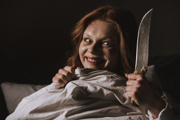 demoniacal smiling girl holding knife in bed