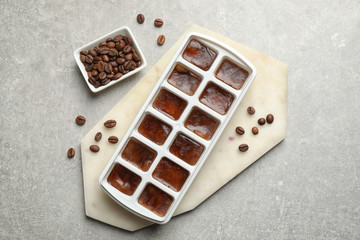 Ice cubes in tray and coffee beans on grey table, flat lay