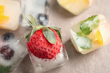 Ice cubes with different berries and mint on grey table, closeup
