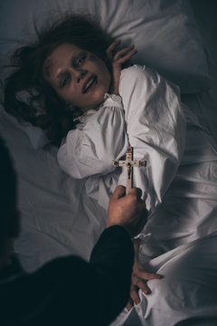 exorcist holding cross over demonic girl in bed