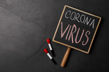 Chalkboard with phrase CORONA VIRUS and test tubes on black background, flat lay. Space for text
