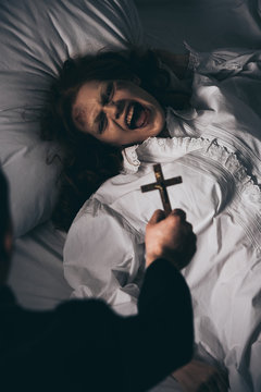 Exorcist holding cross over creepy screaming demon in bed