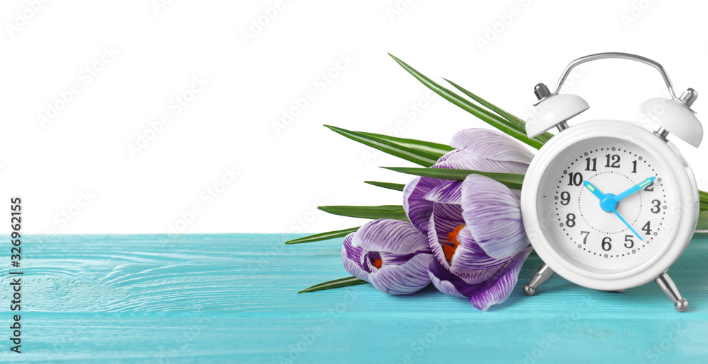 Poster alarm clock and spring flowers on wooden table against white background, space for text. time change