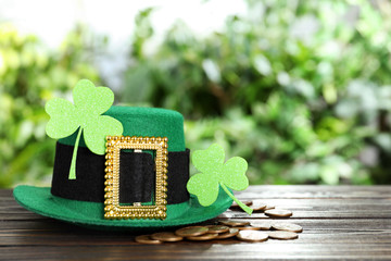 Green leprechaun hat, clover leaves and gold coins on wooden table, space for text. St Patrick's...