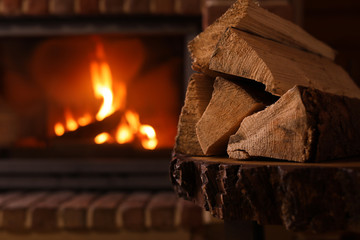 Pile of wood and blurred fireplace on background, space for text. Winter vacation - Powered by Adobe