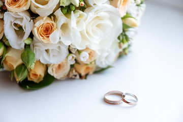 wedding rings and the bride's bouquet are on a white table. close up