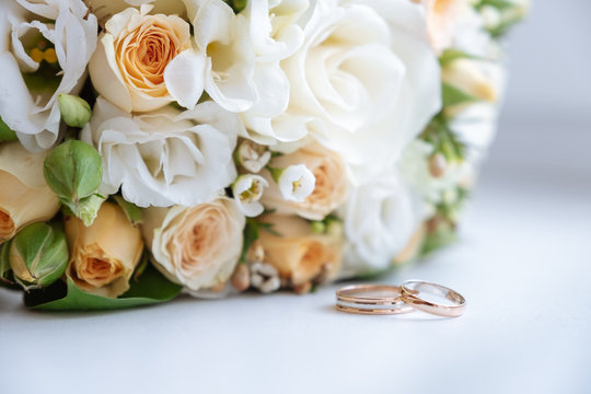 wedding rings lie in front of the wedding bouquet on a white table. close up