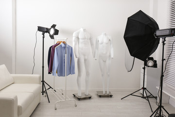 Ghost mannequins, clothes and professional lighting equipment in modern photo studio