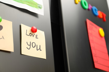 Note with phrase LOVE YOU and magnets on refrigerator, closeup
