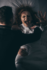 exorcist holding yelling female demon in bed