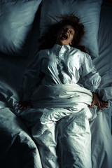 top view of female demon in nightgown screaming while lying in bed